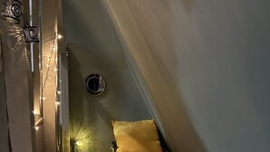 A small, cozy room with a sloped ceiling, a bed with floral bedding, a nightstand with a lamp, and string lights. - Cameo Tree Top Chalet - HOT TUB and Pet Friendly (Jasper)