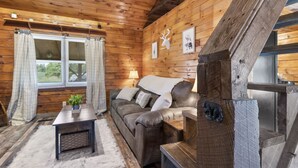 Interior acogedor de una cabaña con techo de madera, un sofá, una mesa y una ventana con cortinas.