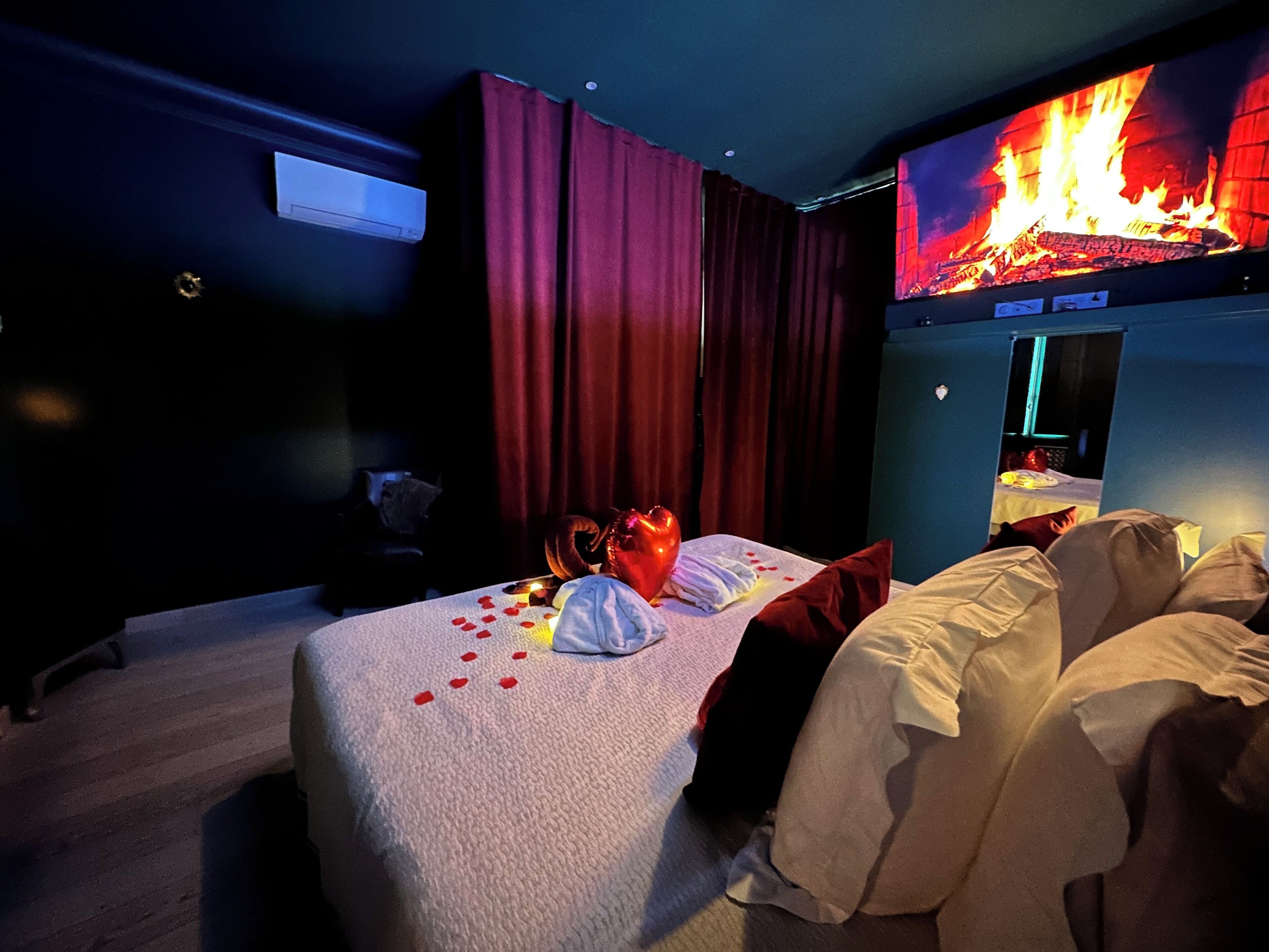 Una habitación de hotel con una cama, una televisión mostrando un fuego y una ventana.