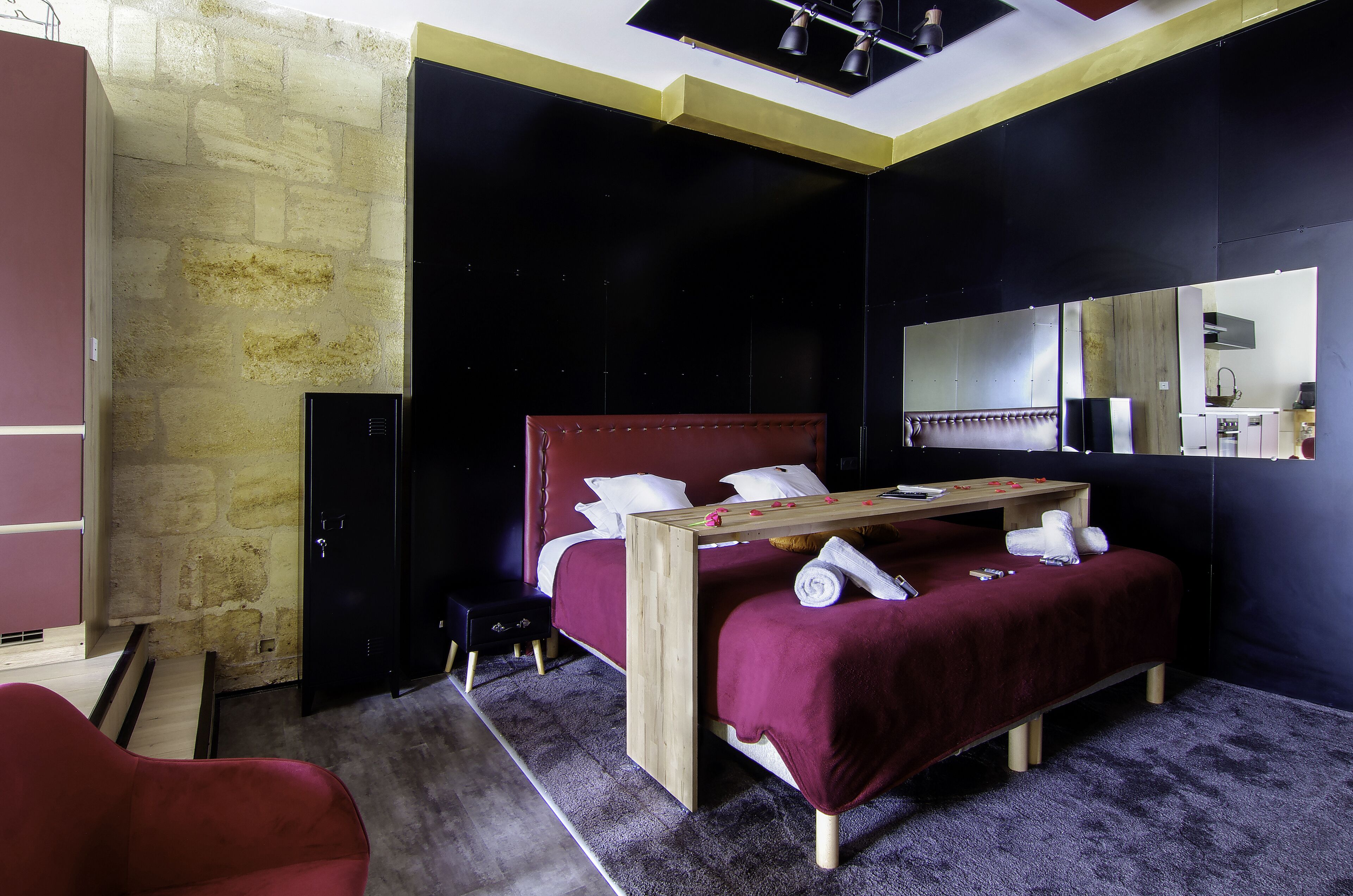 Un dormitorio moderno con pared de piedra, cama roja, mesita de noche de madera y un espejo.