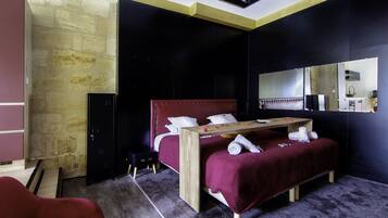 Un dormitorio moderno con pared de piedra, cama roja, mesita de noche de madera y un espejo.