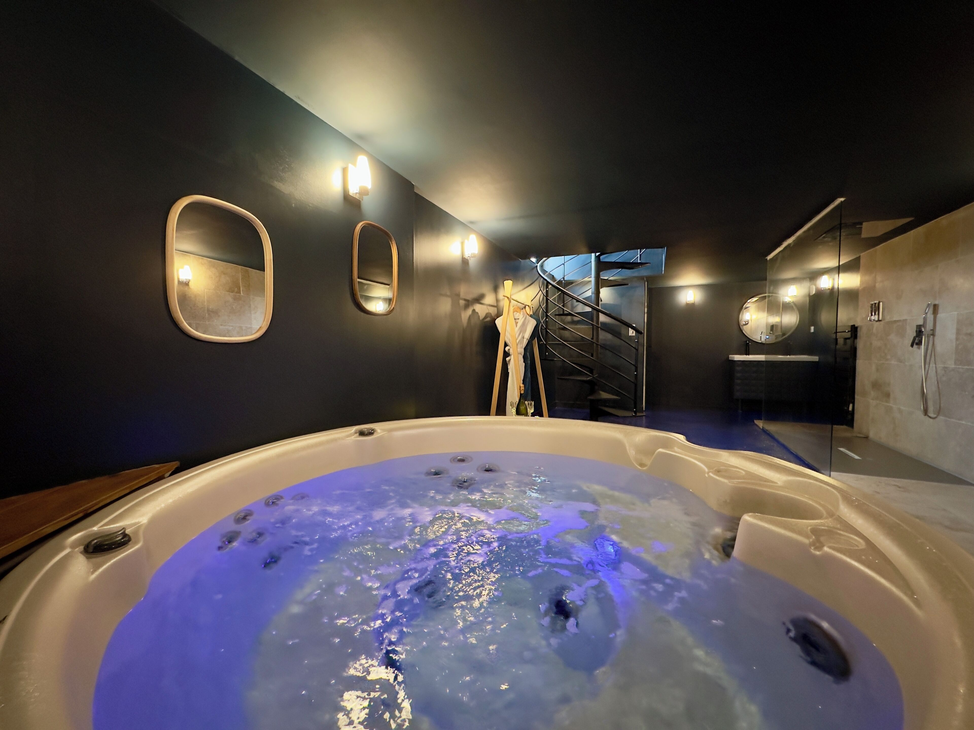 A modern bathroom with a large bathtub, a glass-enclosed shower, and a staircase leading to an upper level.