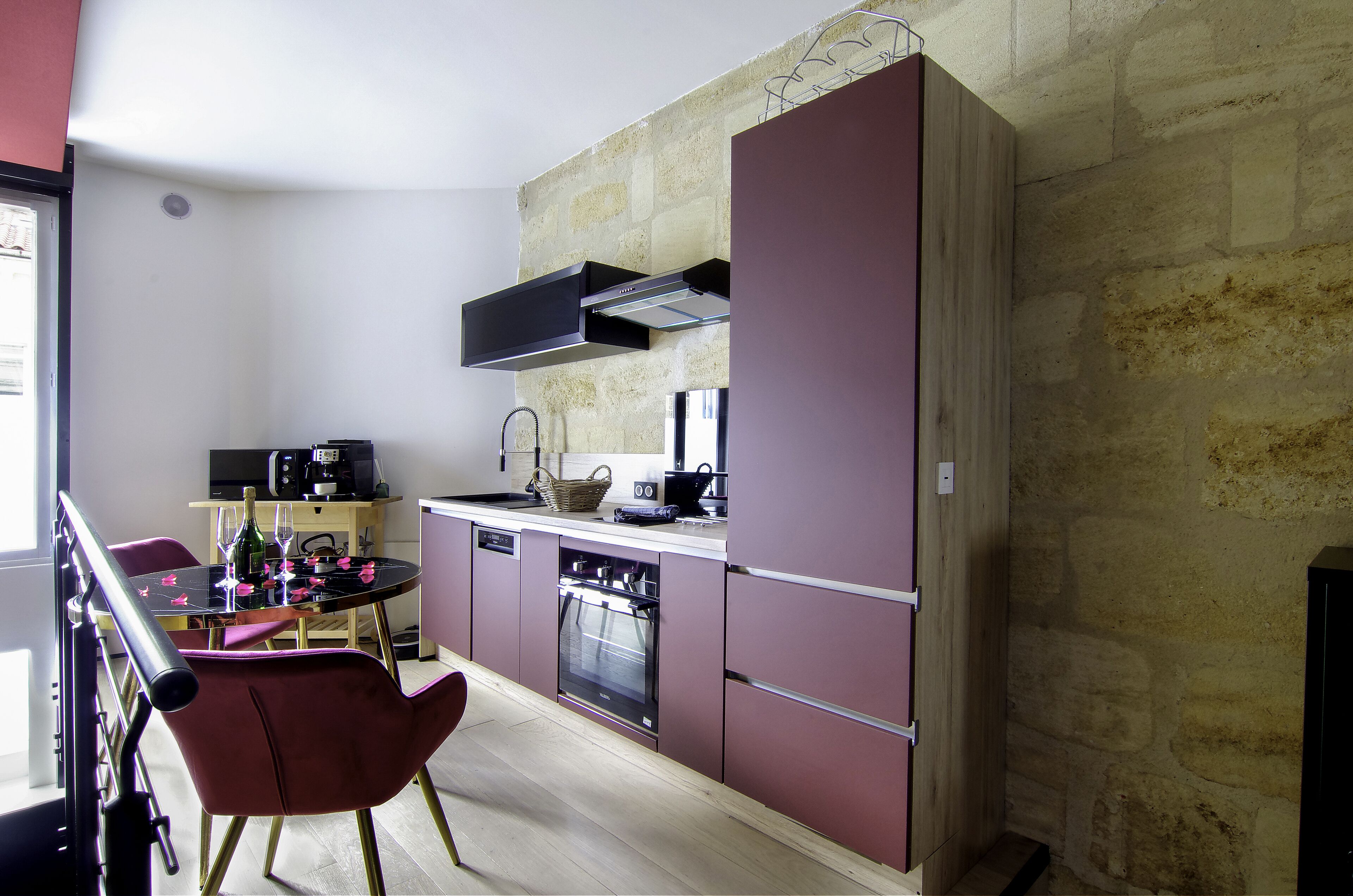 Una cocina compacta con pared de piedra, un comedor con mesa y sillas, y un horno empotrado.
