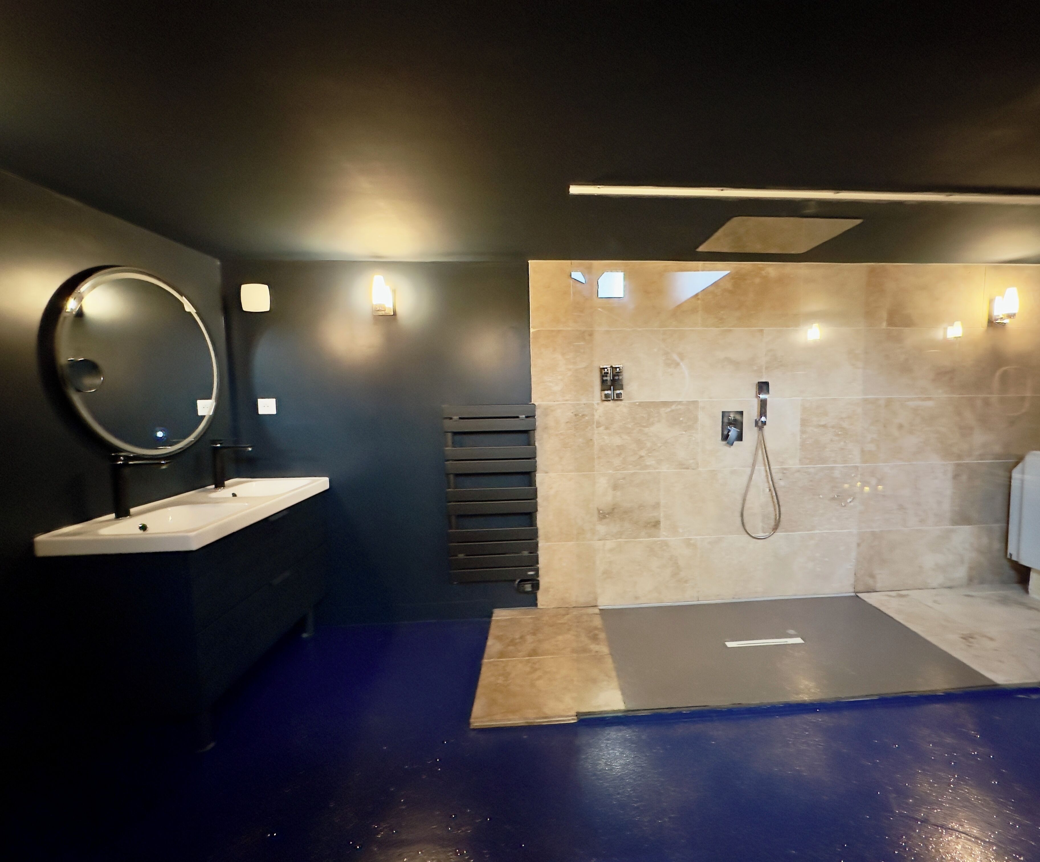 A modern bathroom with a large mirror, two sinks, a shower, and a towel rack.