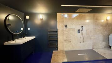 A modern bathroom with a large mirror, two sinks, a shower, and a towel rack.