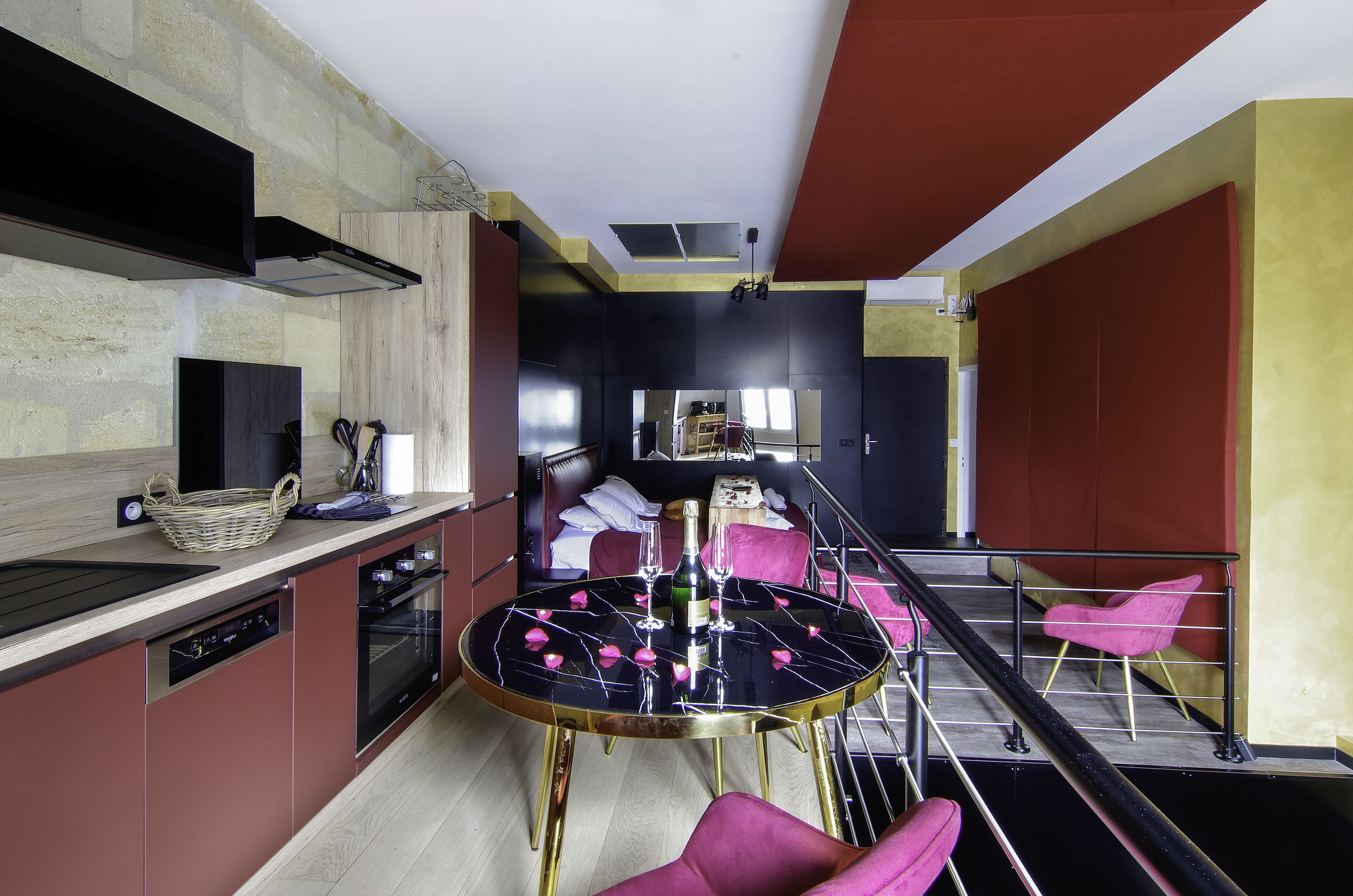 A modern kitchen with a dining area, including a round table with rose petals, a basket, and a bottle.