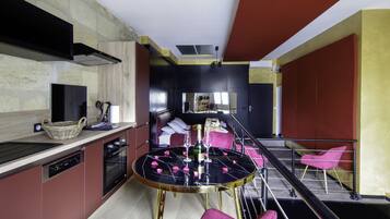A modern kitchen with a dining area, including a round table with rose petals, a basket, and a bottle.