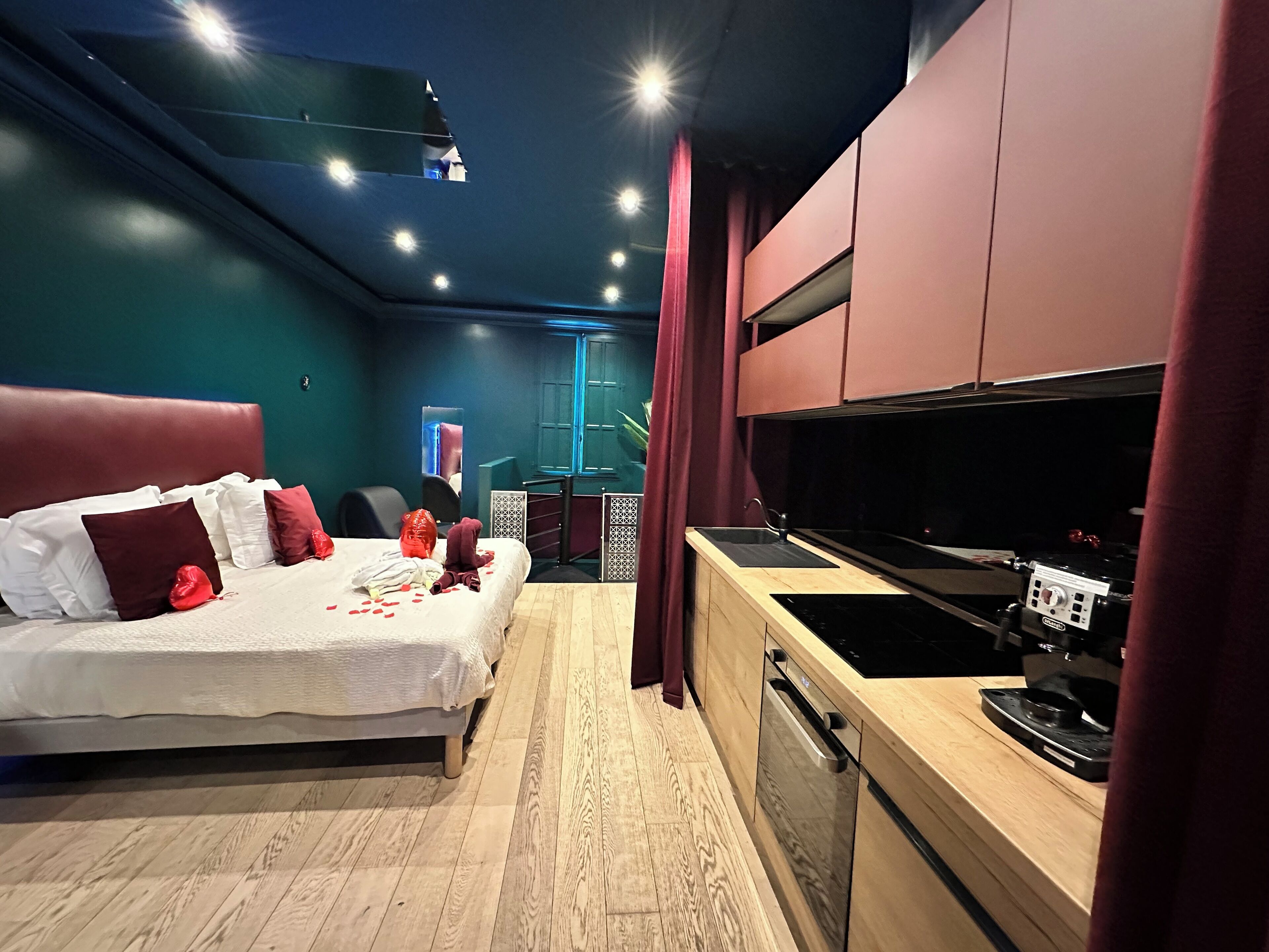 Ein modernes Schlafzimmer mit großem Bett, einer separaten Küchenzeile und Blick auf die beleuchtete Stadt bei Nacht.