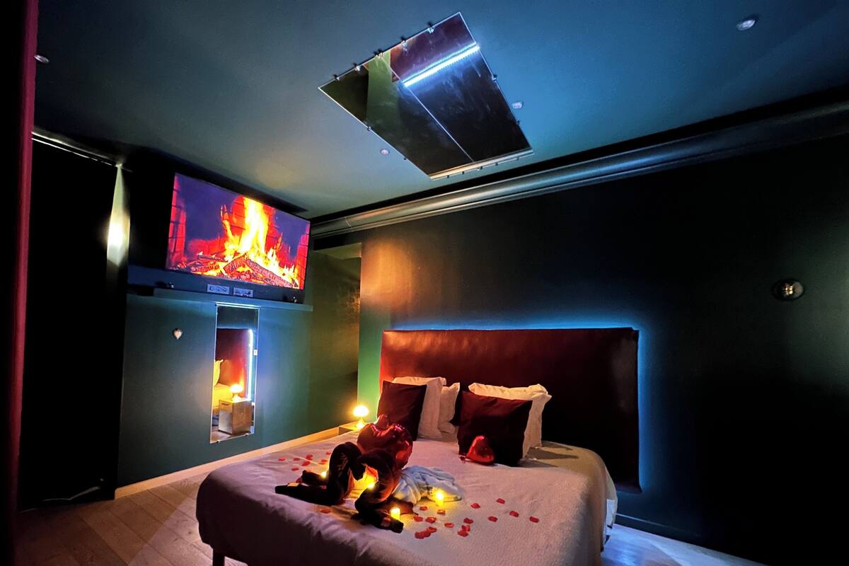 A modern bedroom with a large bed, a TV mounted on the wall, and a ceiling light fixture.