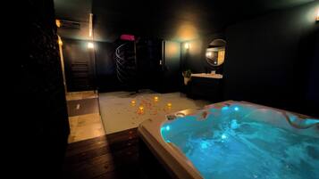 A dimly lit spa area with a hot tub, wooden flooring, and a small seating area.