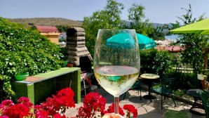A glass of white wine held in front of a table with red flowers, with a green umbrella and outdoor seating in the background. - Apartment in Žaborić with Seaview, Balcony, Air condition, WIFI (5177-1) (Šibenik)