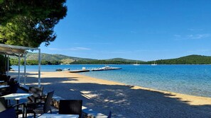 A beachside restaurant with outdoor seating, a dock with boats, and a view of a lake with hills in the background. - Apartment in Žaborić with Seaview, Balcony, Air condition, WIFI (5177-1) (Šibenik)