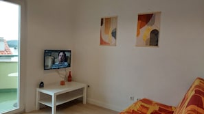 Una stanza con una televisione a muro, un tavolo bianco e due dipinti astratti.