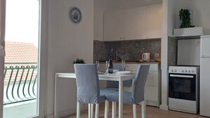 A modern kitchen with white cabinets, a dining table with chairs, a small oven, and a view of a balcony with a railing. - Apartment in Žaborić with Seaview, Balcony, Air condition, WIFI (5177-2) (Šibenik)