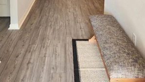 A narrow hallway with wooden flooring, a bench, a small table, and a sofa.