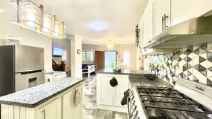 A modern kitchen with granite countertops, a gas stove, and a dining area with a white table and chairs. - Villa Rodriguez Jarabacoa La Vega 3bedroom Hot Jacuzzi (Jarabacoa)
