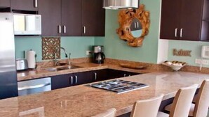 A modern kitchen with dark cabinets, a large island with bar stools, and a stainless steel range hood. - 2BR-2BA Heart of Romantic Zone + Infinity pool (Puerto Vallarta)