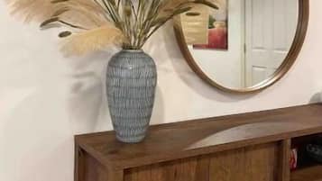 A wooden cabinet with a mirror above it, a vase with dried pampas grass, and a door in the background.