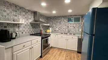 A kitchen with white cabinets, a stove, a sink, and a blue refrigerator.