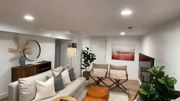 A modern living room with a sofa, ottoman, and armchairs, a small round table, and a potted plant.