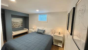 A bedroom with a bed, bedside tables, a bench, and artwork.