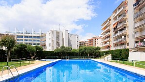 A swimming pool surrounded by apartment buildings, with a clear sky above. - FABRA Apartment (Salou)
