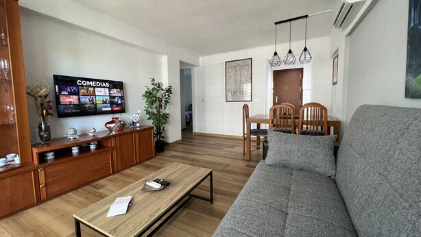 A living room with a grey sofa, wooden coffee table, and a TV displaying 'COMEDIAS'. - FABRA Apartment (Salou)