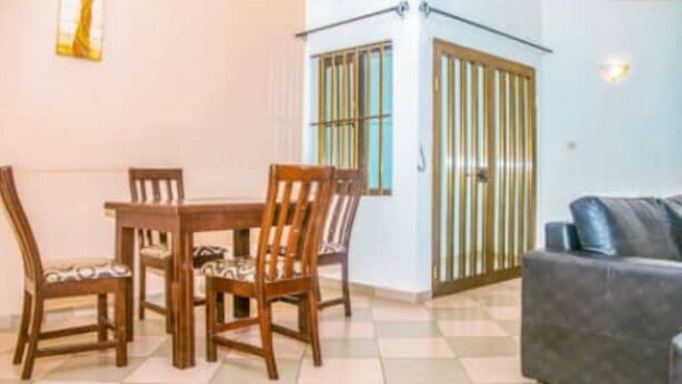 Un coin repas avec une table et des chaises en bois, un canapé et une vue sur l’extérieur par une fenêtre équipée de stores verticaux.
