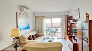Habitación de hotel con sofá, una mesita de centro, lámpara, estantería y un ventanal con vistas al exterior.