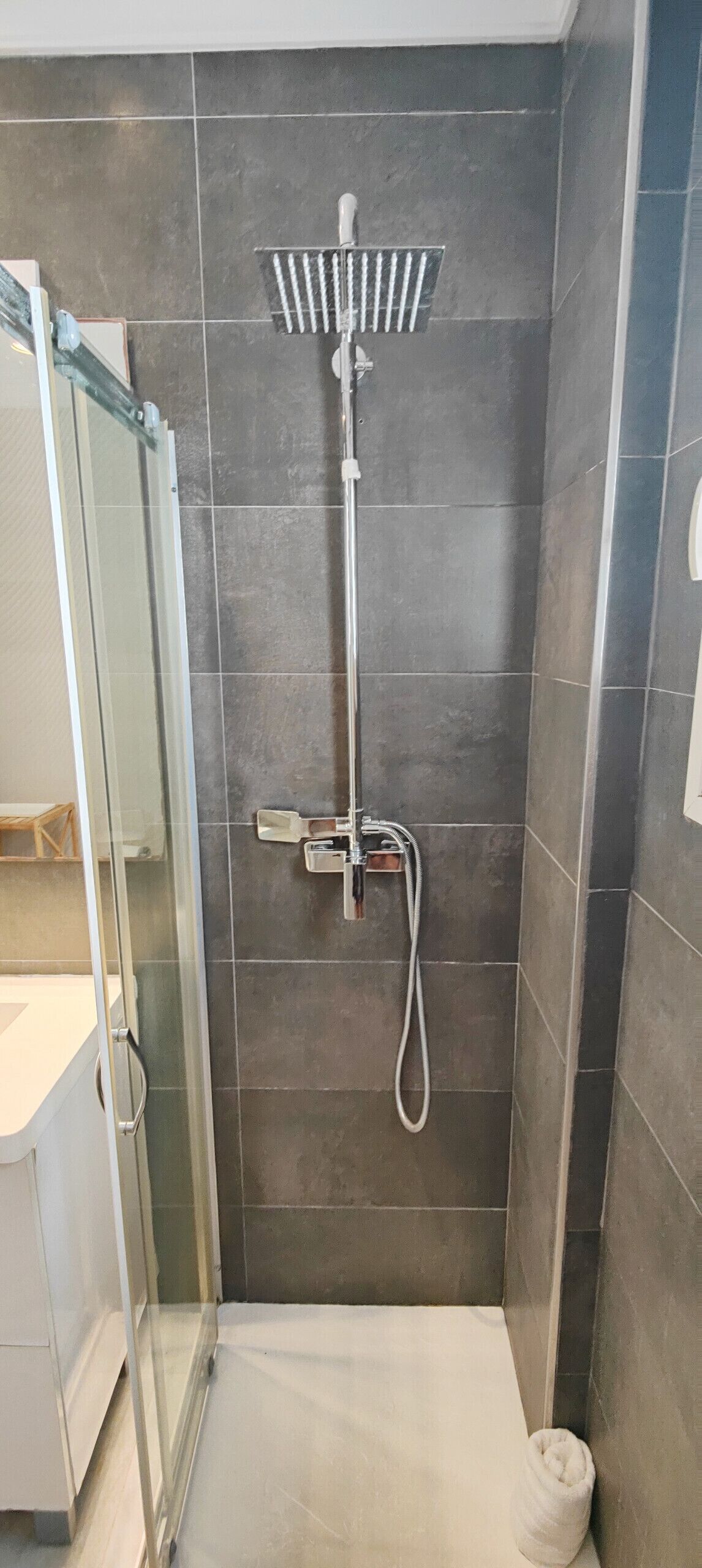 Une douche avec une porte en verre, un pommeau de douche à main et un robinet mural.