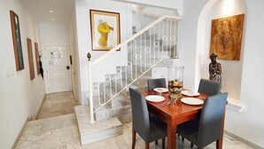 Un comedor con una mesa de madera dispuesta para cuatro, una escalera con barandillas blancas y obras de arte en las paredes.