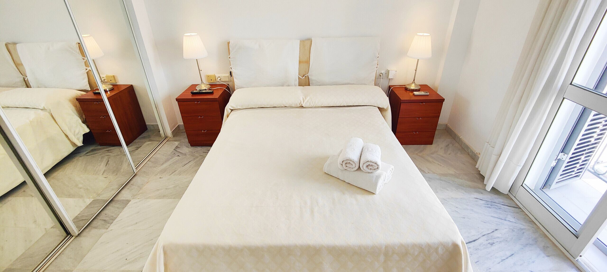 A hotel room with a large bed, two bedside tables with lamps, a mirror, and a window with curtains.