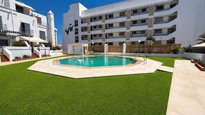 A swimming pool surrounded by artificial grass, with a white building in the background.