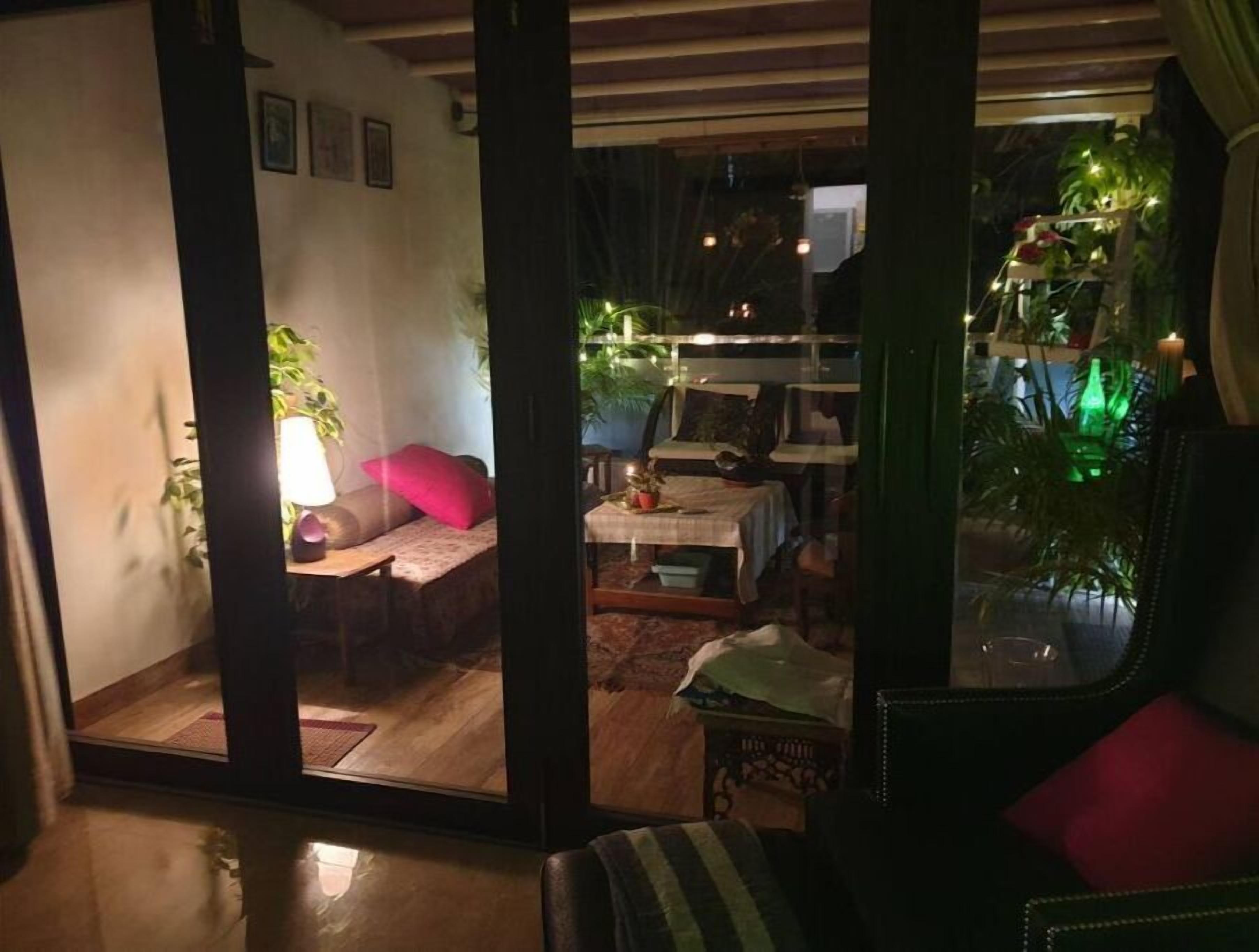 A cozy living room with a sofa, a table, and a chair. There are plants and a lamp.