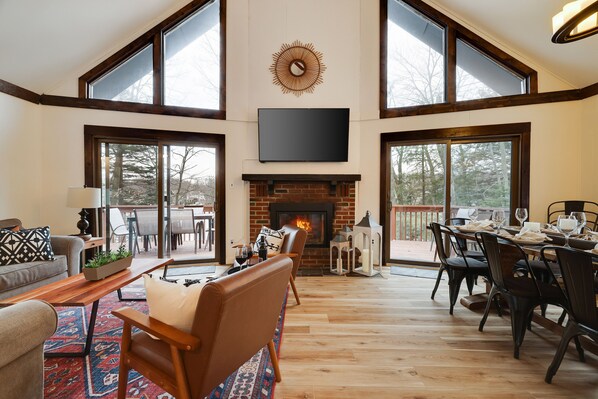A spacious living room with a fireplace, large windows, and a dining area.
