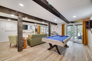 A modern living room with a pool table, a green sofa, and a wooden ceiling.
