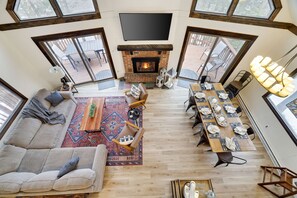 Un amplio salón con chimenea, un sofá, una mesa de comedor lista para seis personas y ventanas grandes.