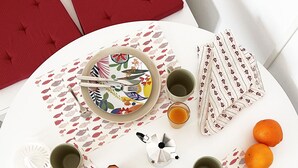 A round dining table with plates, cutlery, and a coffee pot, surrounded by chairs and a red couch. - Mysa - Your home 5 min from the airport (Isola Sacra)