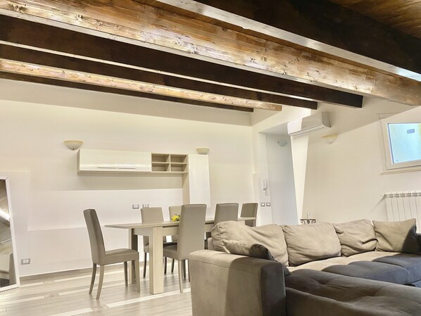 A modern living room with a wooden ceiling, a dining area with a table and chairs, and a large beige sofa. - La Dimora Del Golfo (Gaeta)