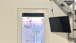 A room with a window overlooking a street, a mounted television, and a staircase. - La Dimora Del Golfo (Gaeta)