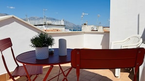 A small outdoor seating area with a table and chairs, a potted plant, and a view of the sea and mountains in the background. - La Dimora Del Golfo (Gaeta)