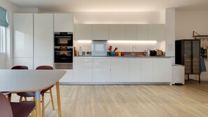 Et moderne køkken med hvide skabe, en central ø og et spiseområde med et bord og stole.