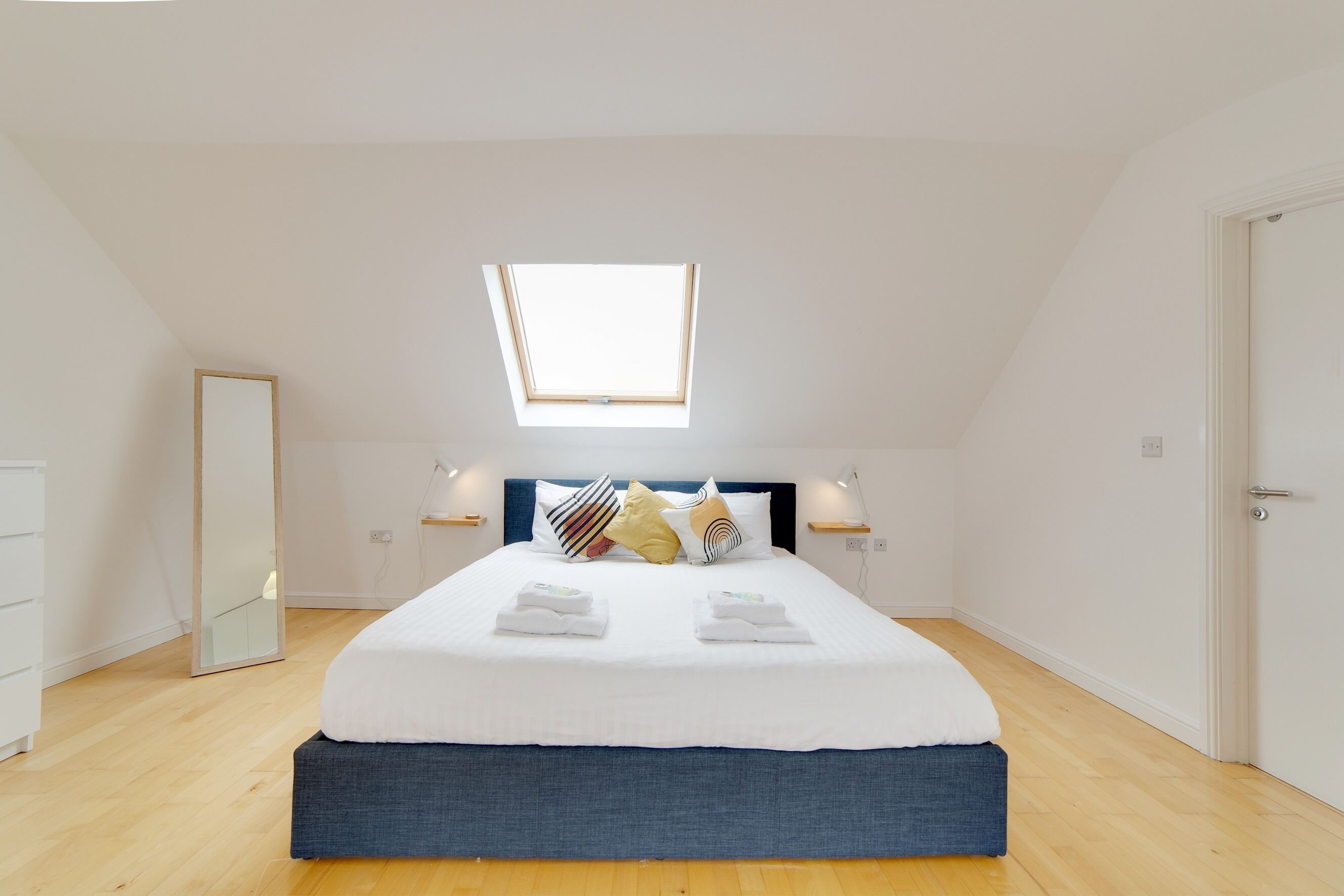 Ein Schlafzimmer mit Dachfenster, einem Bett mit weißen Leinentüchern, einem blauen Kopfteil und Holzboden.