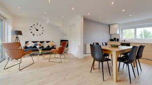 A modern living room with a sofa, chairs, a dining table, and a wall clock. - Pass the Keys | 49 Byron Square Modern and Spacious 3 Bed Home with Free Parking (Cambridge)