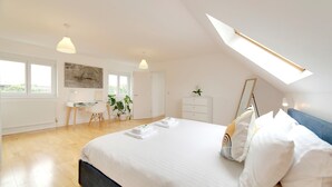 A bedroom with a large bed, a desk, and a chair, a skylight, and a view of greenery outside. - Pass the Keys | 49 Byron Square Modern and Spacious 3 Bed Home with Free Parking (Cambridge)