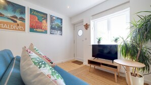 A living room with a blue sofa, a TV on a wooden stand, and a potted plant. - Pass the Keys | Modern & Spacious 1 Bed Terrace with Free Parking (Cambridge)