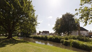 A riverside view with a grassy area, trees, and buildings in the background. - Pass the Keys | 19th Century Barn with Free Parking (Histon)