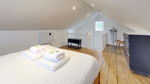 A spacious attic bedroom with a large bed, wooden floor, a small table, and a wardrobe. - Pass the Keys | 19th Century Barn with Free Parking (Histon)