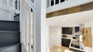 A modern kitchen with a central island, white cabinetry, and a wooden beam ceiling. - Pass the Keys | 19th Century Barn with Free Parking (Histon)
