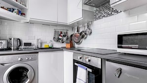 A modern kitchen with white cabinetry, a built-in washing machine, a microwave, and a stove. - Spacious London Flat | Near Primrose Hill & Camden - Pass the Keys (London)